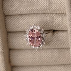 a pink diamond ring sitting on top of a white cloth covered cushioned box,