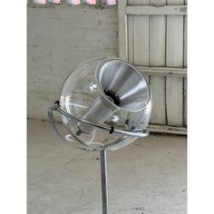 a metal and glass object sitting on top of a metal stand in front of a white brick wall