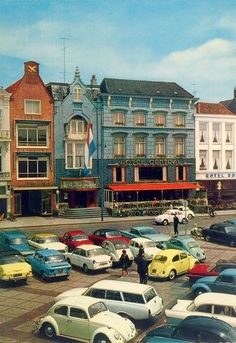 an old photo of cars parked in front of buildings and people walking around the street