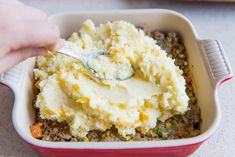 a person scooping mashed potatoes into a casserole dish