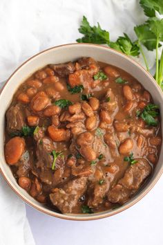 a bowl filled with meat and beans on top of a white cloth next to cilantro