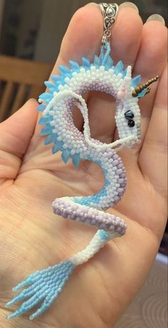 a hand holding a tiny blue and white beaded dragon keychain in it's palm