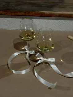 two glasses of wine are sitting on a table with a ribbon around them and a bottle of wine in the background