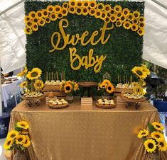 a table topped with sunflowers and desserts under a tented sign that says sweet baby