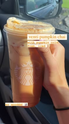 a person holding up a cup of pumpkin chai in front of a car window