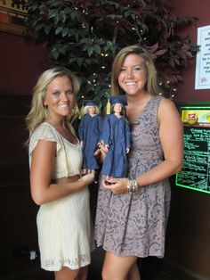 two women standing next to each other in front of a tree with dolls on it