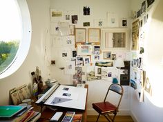 a room with a desk, chair and many pictures on the wall above it in front of a round window