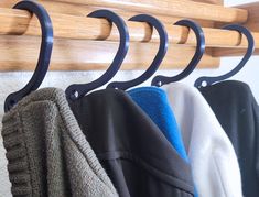 three coats hanging from hooks on a coat rack with sweaters in the foreground