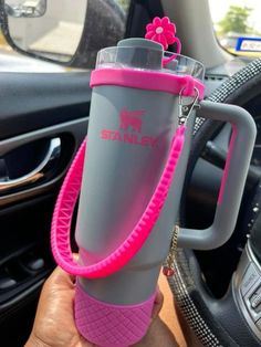 a person holding a pink and gray cup in their hand while sitting in a car