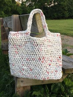 a white crocheted bag sitting on top of a wooden bench in the grass