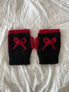 two knitted mitts with red bows on them sitting on a white bed sheet