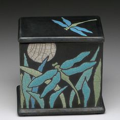 a black box with blue and green designs on the lid is sitting in front of a gray background