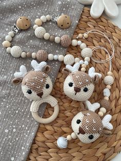 two knitted deer keychains are sitting on a woven tablecloth with beads and wooden bead necklaces