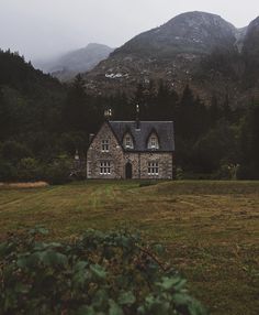 an old stone house in the middle of a field with mountains in the back ground