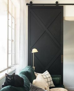 a black cat sitting on top of a green couch next to a lamp and window