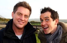 two men standing next to each other in front of a fence and grass covered field