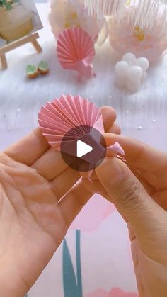 a person holding a pink paper fan in their hand with other items on the table behind them