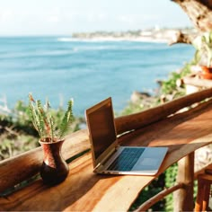 an open laptop computer sitting on top of a wooden table next to a potted plant