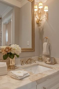 a bathroom sink sitting under a mirror next to a white counter top with flowers on it