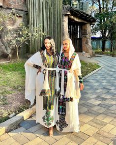 two women standing next to each other near a tree