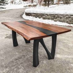 a wooden table sitting on top of snow covered ground next to a stone wall and trees