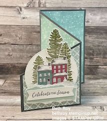 a christmas card with a house and trees in the snow, on top of a wooden table