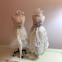 two mannequins dressed in white dresses with bows and lace on them, sitting next to each other