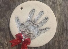 a handprint ornament with a red bow on it sitting on top of a wooden table