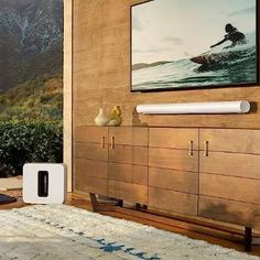 a painting hangs on the wall next to a wooden cabinet with two vases and a surfboard