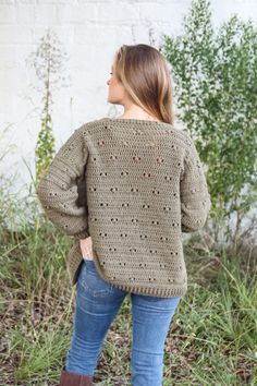 a woman standing in front of a white brick wall wearing a green sweater and brown boots