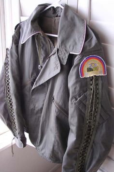 an old leather jacket hanging on a hook in front of a window with a rainbow patch