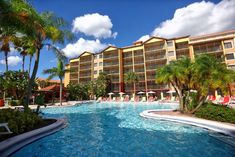 an outdoor swimming pool surrounded by palm trees and lawn chairs in front of a multi - story building