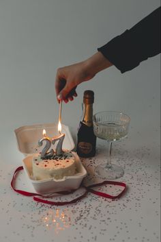 a person lighting a candle on a cake in a box with confetti around it