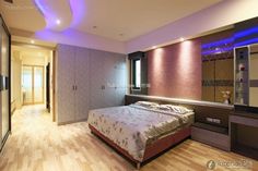 a bedroom with a large bed and purple lighting on the wall above it, along with hardwood flooring