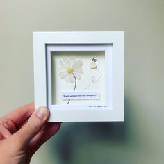 a hand holding a white frame with a flower in it