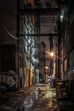 an alleyway at night with street lights and graffiti on the buildings along side it