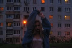 a woman standing in front of a tall building at night with her arms raised up