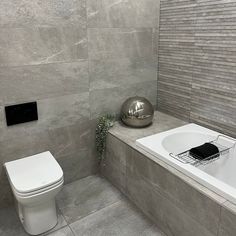 a white toilet sitting next to a bath tub in a bathroom under a tiled wall