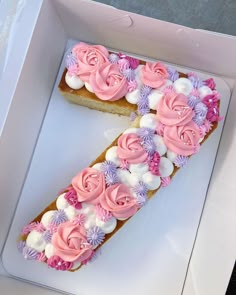 a cake in a box with pink and white frosting flowers on the top is shaped like an letter