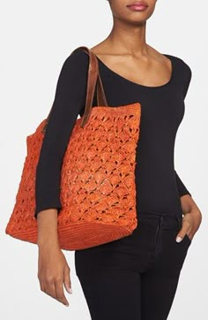 a woman holding an orange crocheted bag