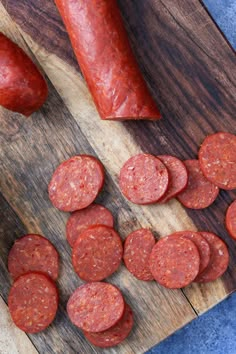 sliced sausages on a wooden cutting board next to a knife and pepperoni slices