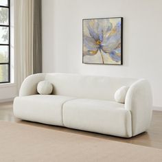 a white couch sitting in front of a window next to a painting on the wall