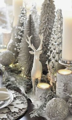 a table topped with silver and white christmas decorations, candles and ornaments on top of it