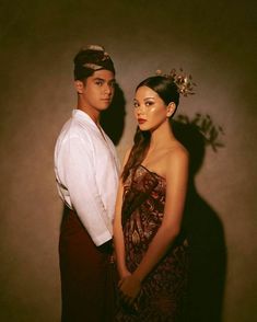 a man and woman standing next to each other in front of a dark background,