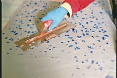 a person in blue gloves and red shirt using a trowel on a floor