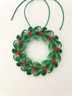 an origami christmas wreath hanging on a green string with red flowers and leaves