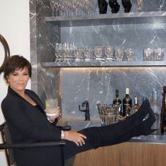 a woman sitting in a chair holding a wine glass next to a bar filled with liquor bottles