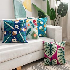 a white couch with colorful pillows on it in front of a potted palm tree