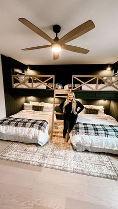 a woman standing next to two beds in a room with wooden ceiling fans and black walls