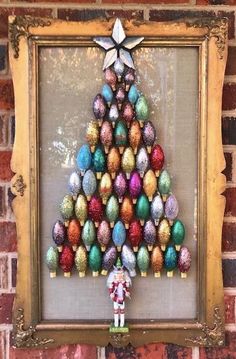 a christmas tree made out of colored eggs in a frame on a brick wall next to a small figurine